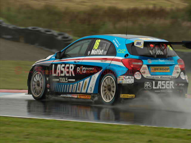 A blue racing car with lots of branding that is racing in rainy weather conditions
