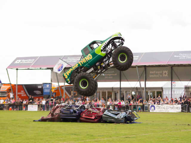 A green monster truck in the air after crushing a bunch of cars