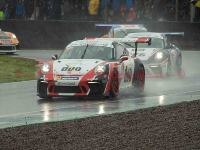 A bunch of racing cars driving in wet conditions, water surrounding them and being lifted from the road