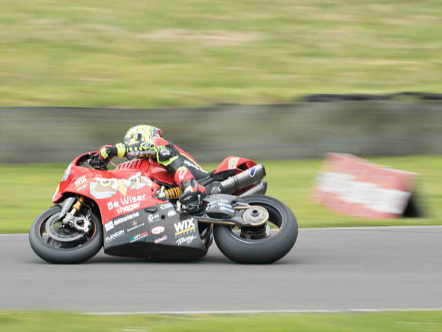 A red motorbike moving very fast on track with blurring surrounding outside of the image